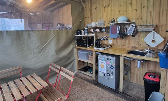 A wooden room with table and chairs and kitchen equipment including a fridge and microwave